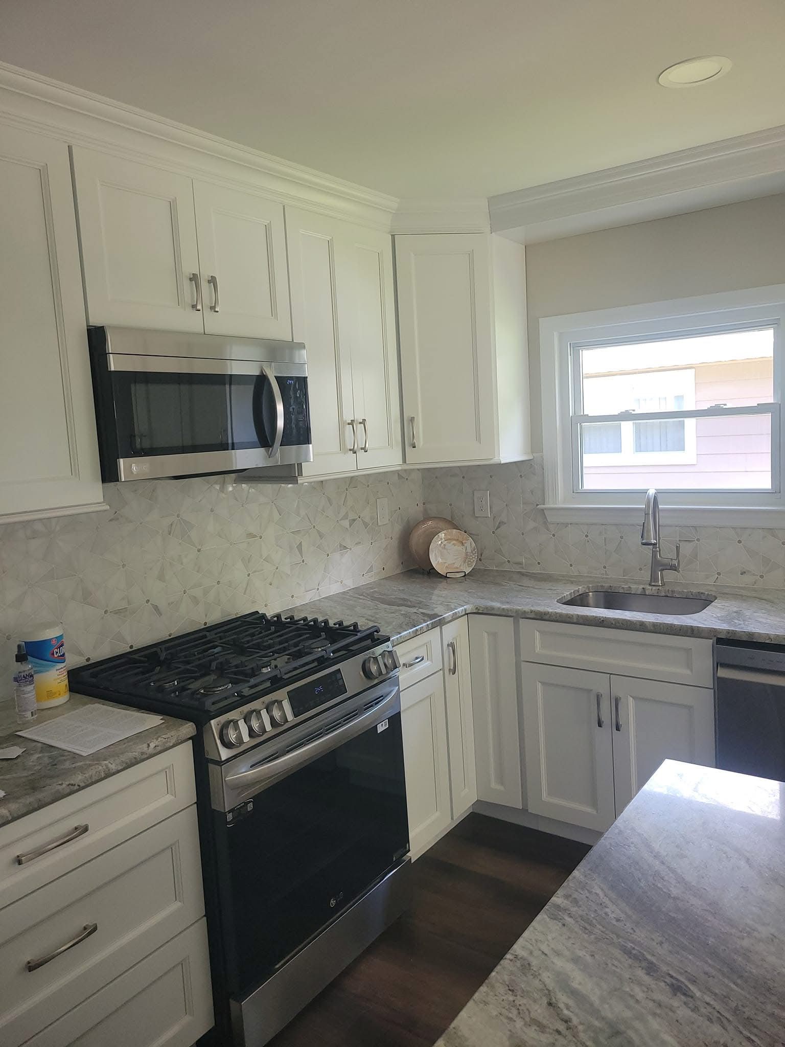 Bright white kitchen with black stove, white cabinets, and granite countertops by a window.