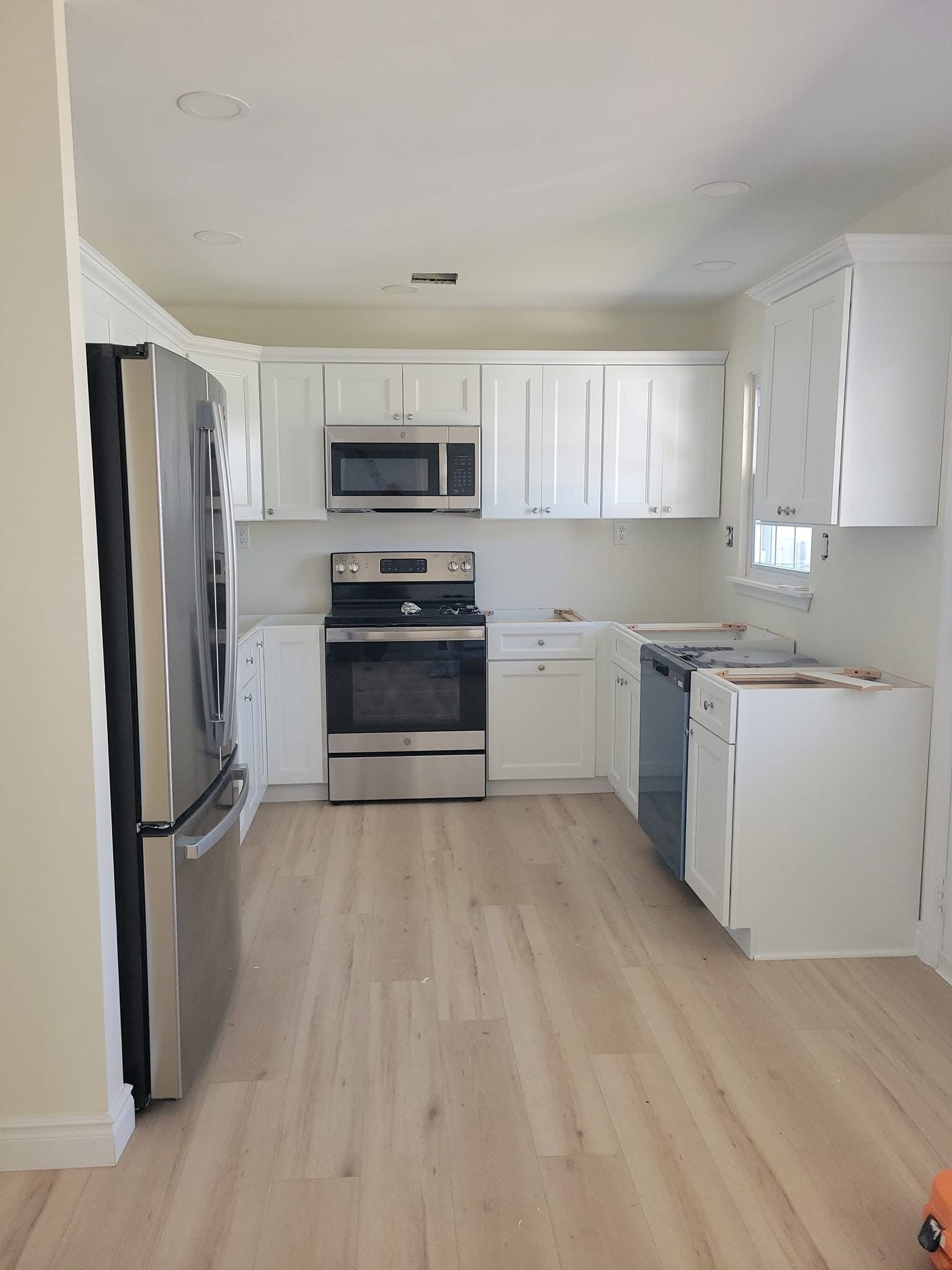 Bright white kitchen with stainless steel appliances, white cabinets, and light wood floors.