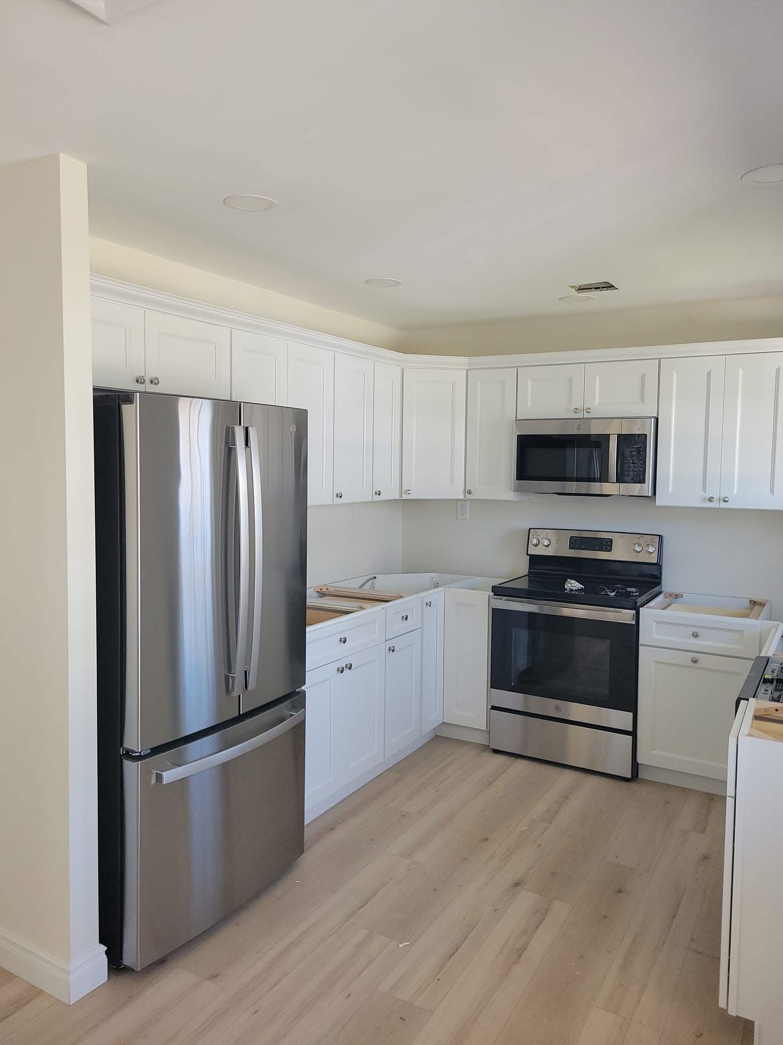 Bright white kitchen with stainless steel appliances, white cabinets, and light wood flooring.