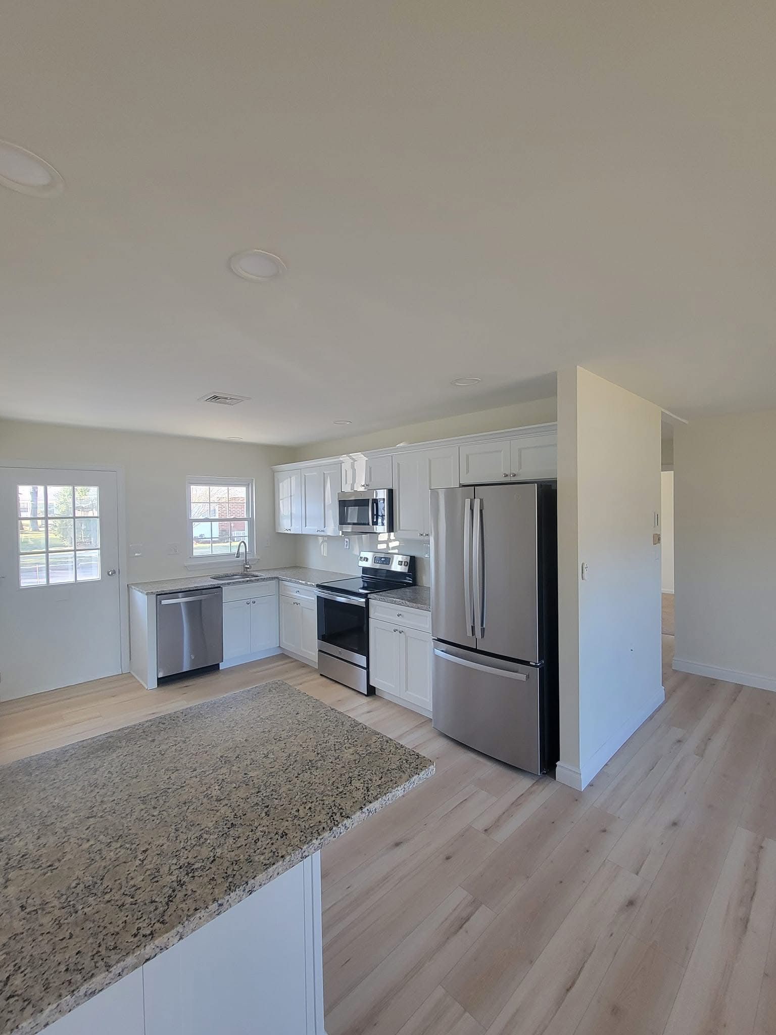 Bright, open kitchen with white cabinets, stainless-steel fridge, island counter, and light wood floors