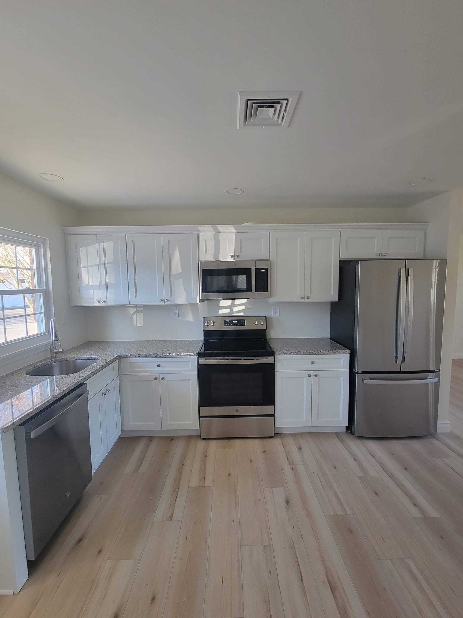 Bright modern kitchen with white cabinets, stainless steel appliances, and light wood floors