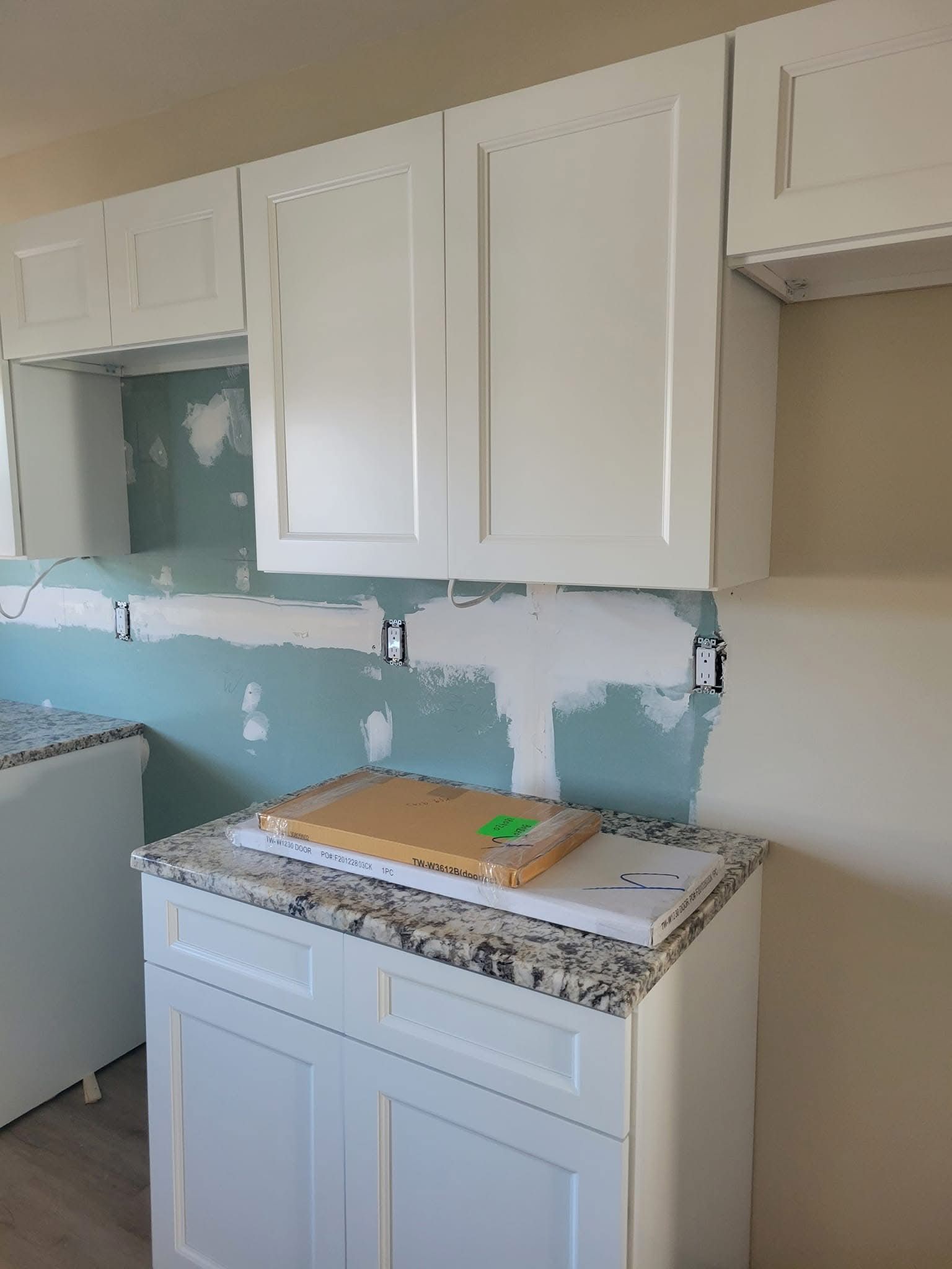 Kitchen cabinets above a sink area with partially removed backsplash and exposed wall under renovation