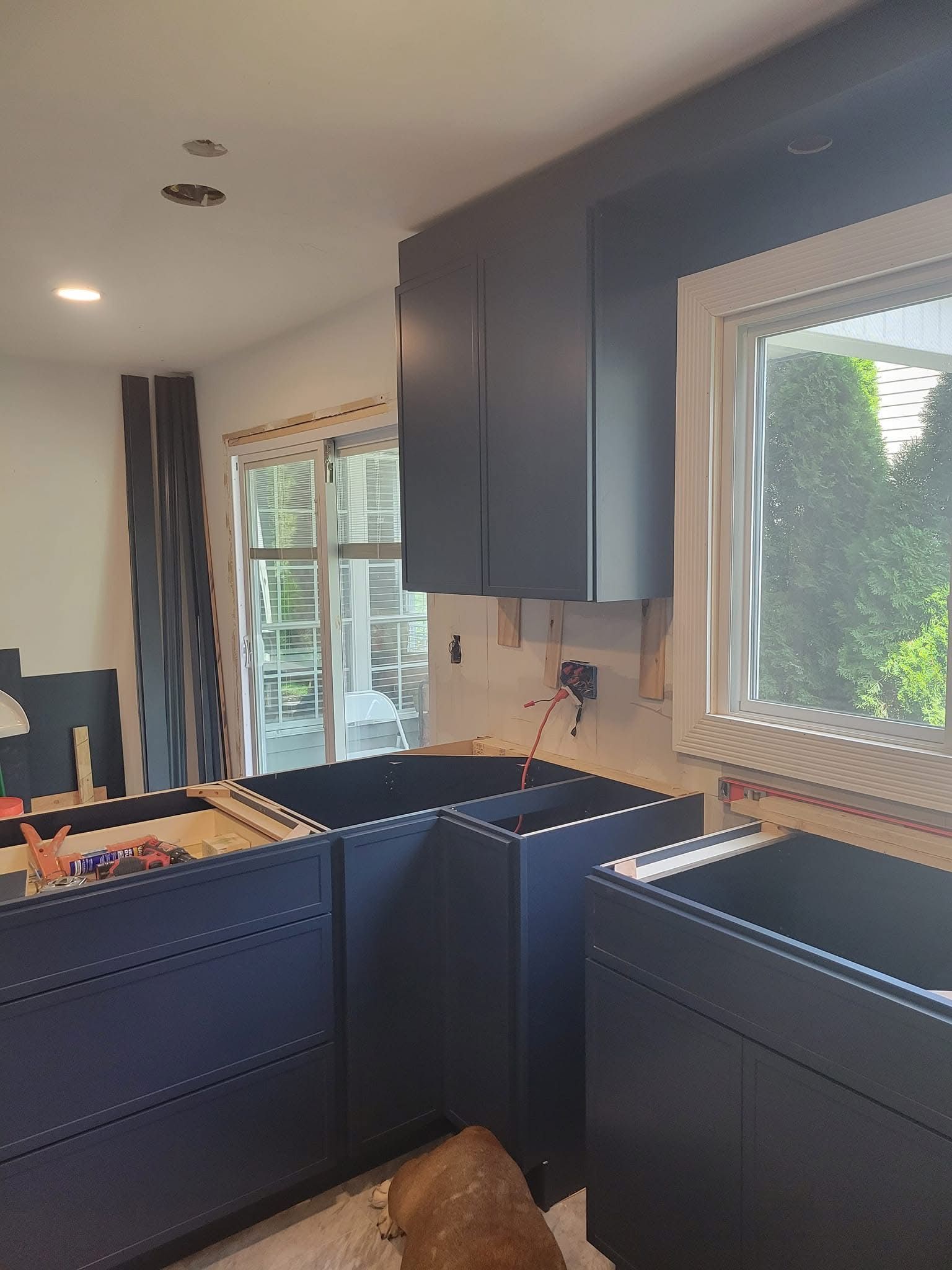 Dark blue kitchen cabinets and island with sink, white countertop, and a window showing greenery.