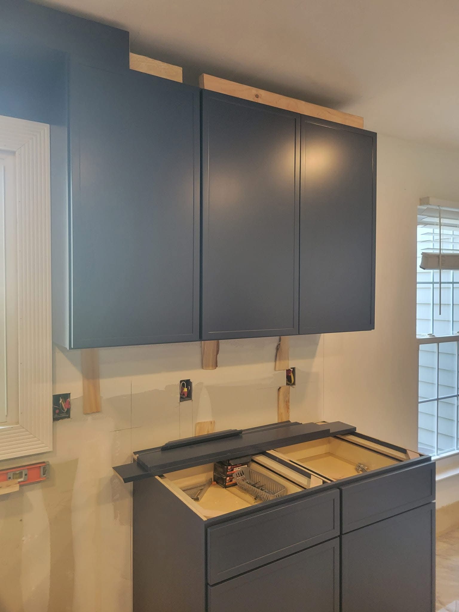 Blue kitchen cabinets above a countertop with a sink and window in a bright room