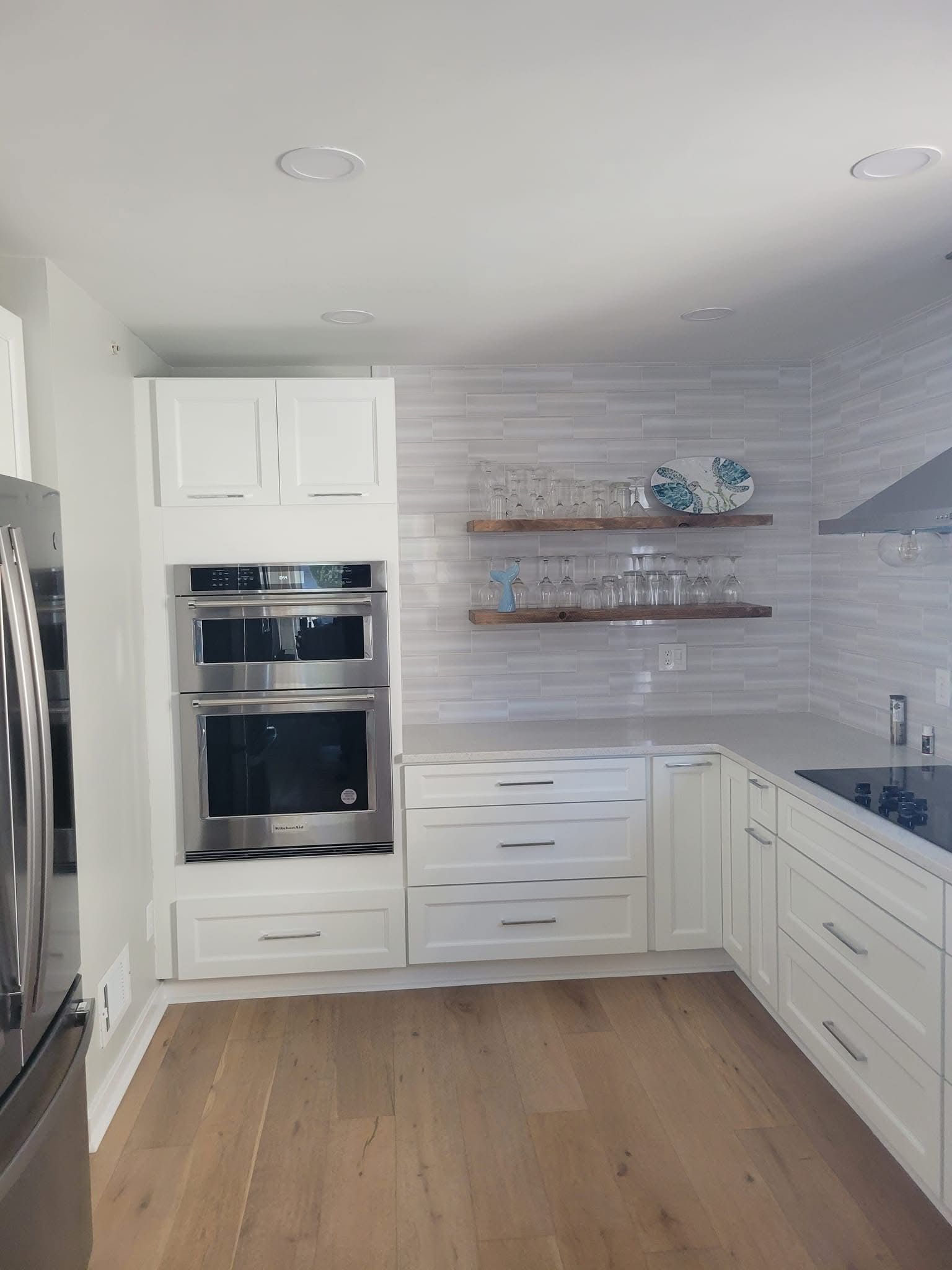 Bright modern kitchen with white cabinets, built-in ovens, wood floor, and open shelves with decor.