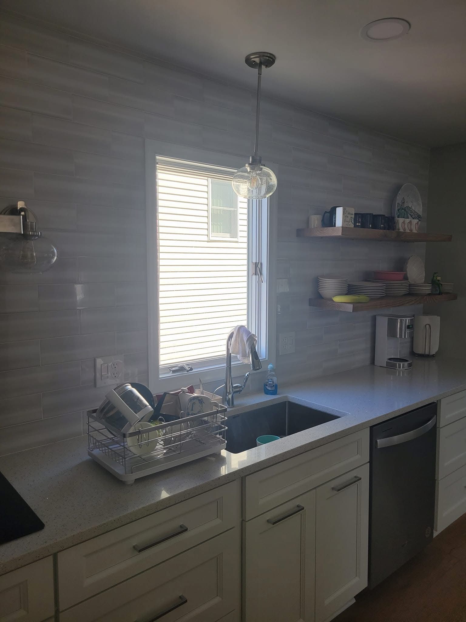 Kitchen with sink, white cabinets, window blinds, shelves, and dishwasher in soft daylight