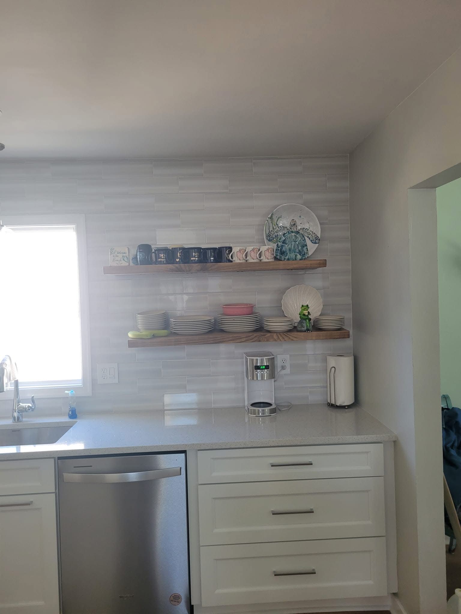 Modern kitchen with white cabinets, stainless dishwasher, open shelves, sink, and bright window light