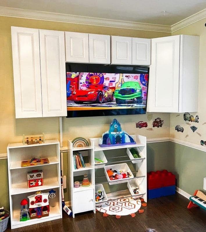 Children's playroom with white shelves, toy bins, and a wall-mounted TV showing Cars characters