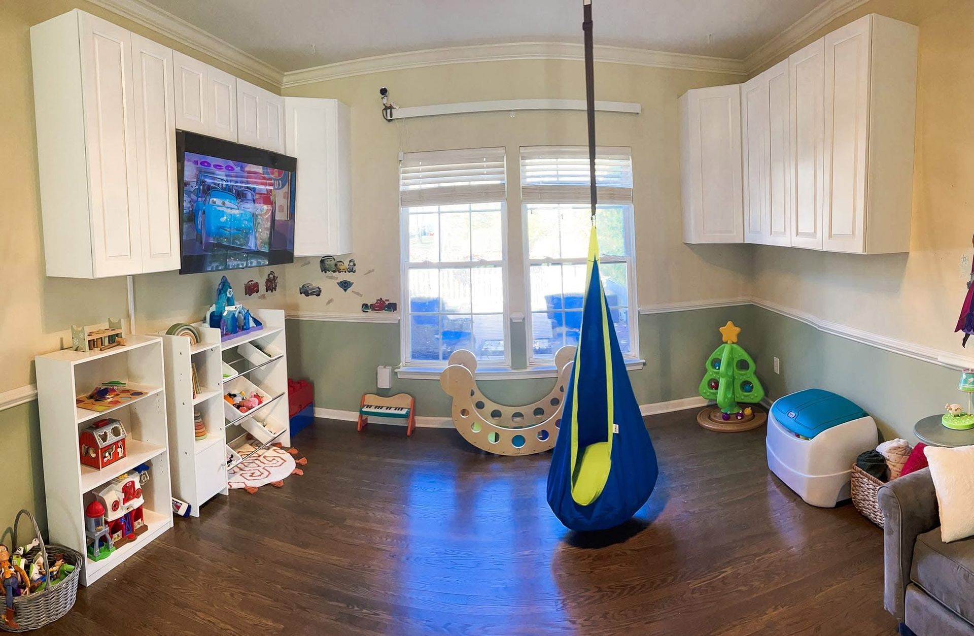 Bright playroom with toys, shelves, hanging swing, and hardwood floor by a window