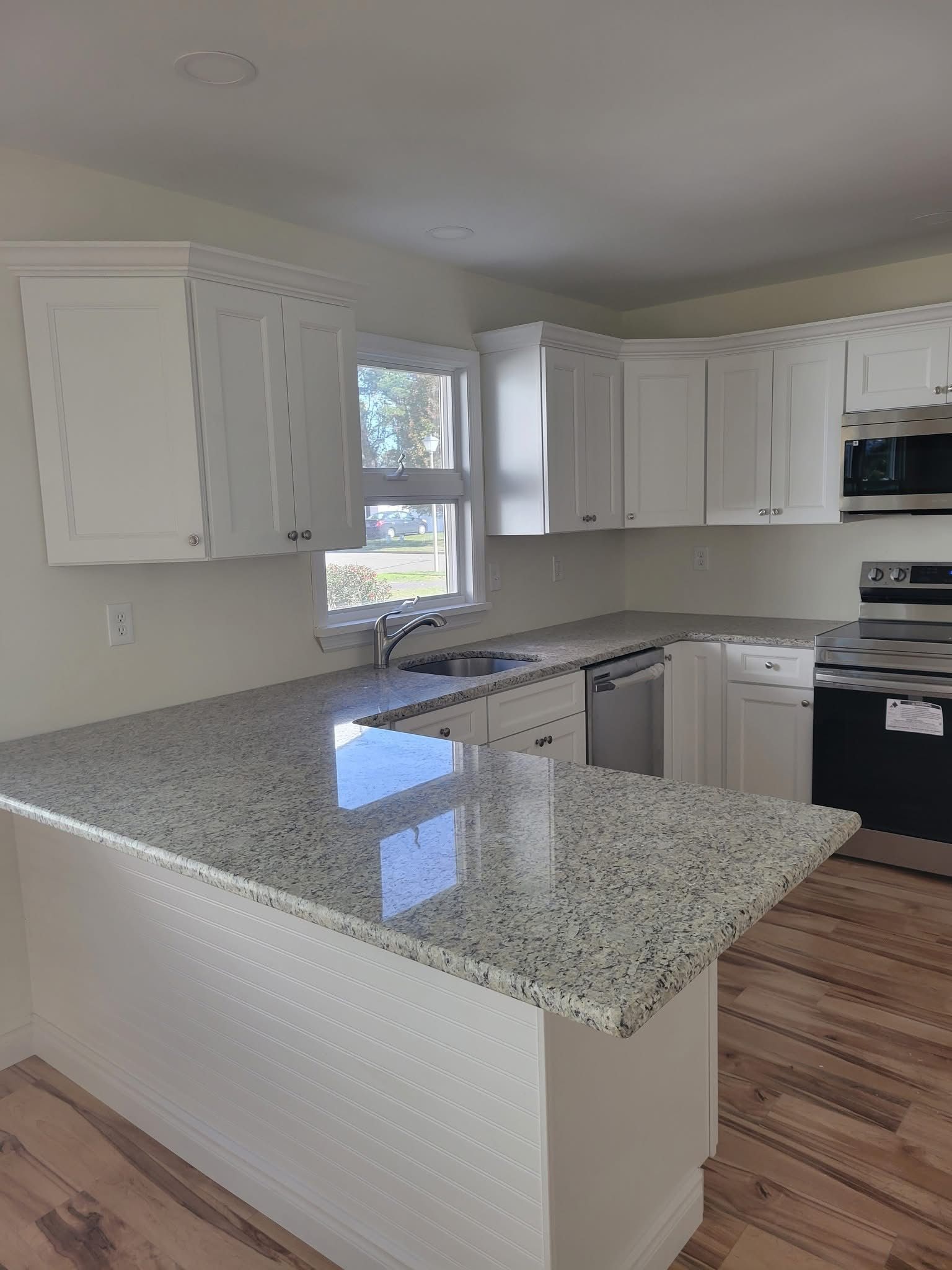 Bright kitchen with white cabinets, speckled granite island, and hardwood floors
