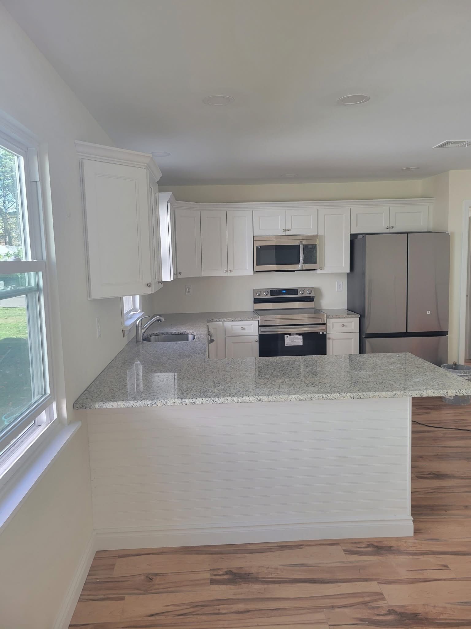 Bright white kitchen with granite island, white cabinets, stainless appliances, and a large window.