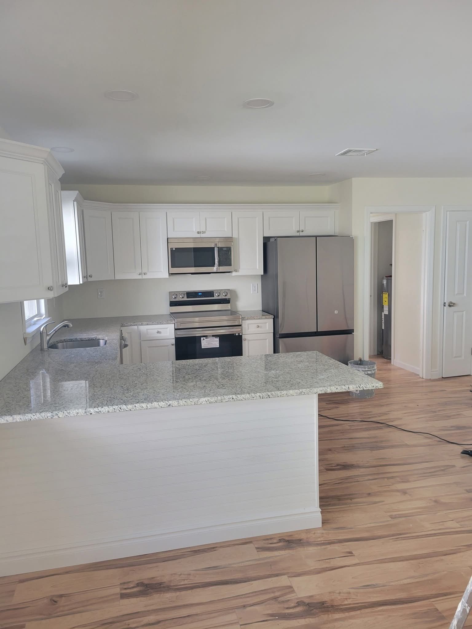 Bright white kitchen with granite island, stainless appliances, and hardwood floors.