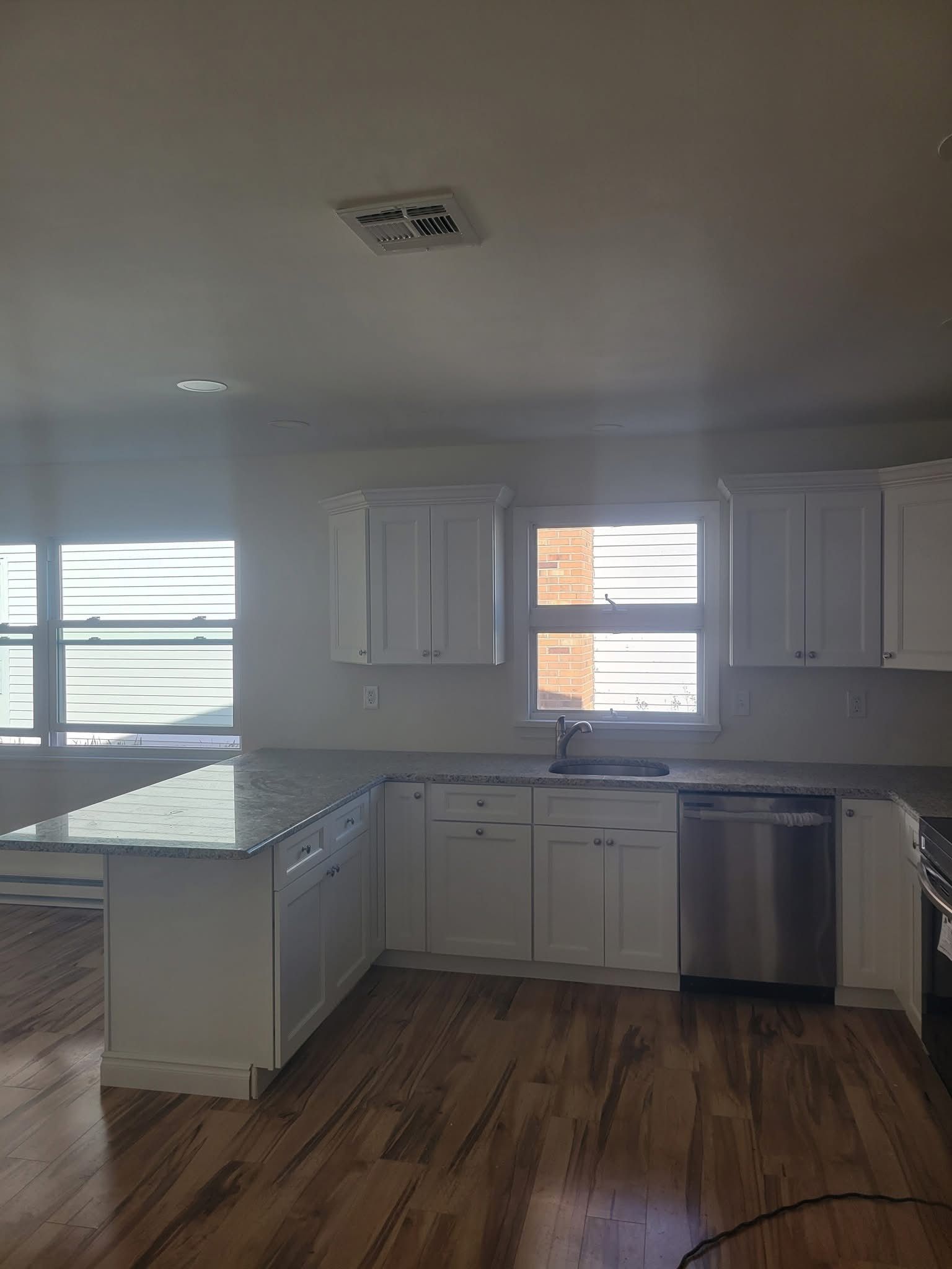 Bright kitchen with white cabinets, granite counters, stainless dishwasher, and hardwood floors.