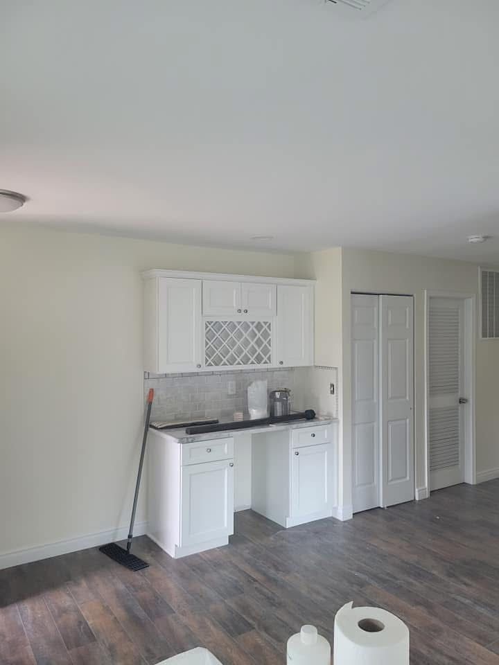 Empty kitchen nook with white cabinets, black countertop, and dark wood flooring.