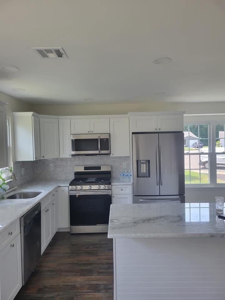 Modern white kitchen with stainless steel appliances, marble island, gray backsplash, and dark wood floor