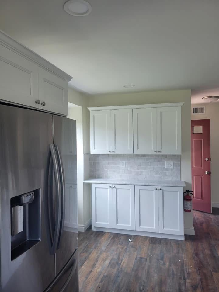 Modern kitchen with stainless steel fridge, white cabinets, tiled backsplash, and wood-look floors