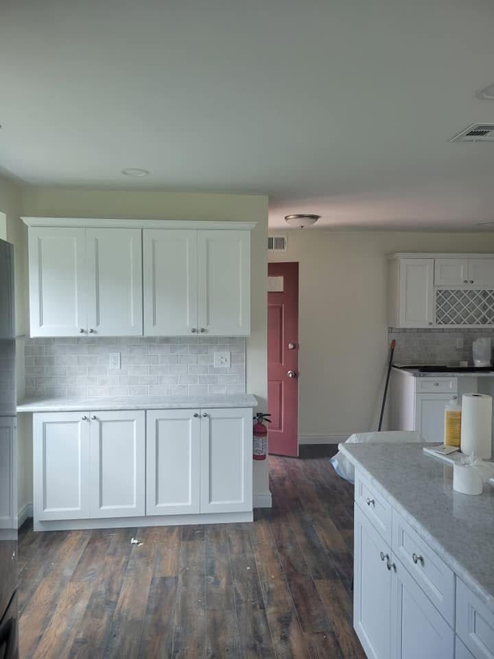 Empty modern kitchen with white cabinets, gray countertops, and wood-look flooring.