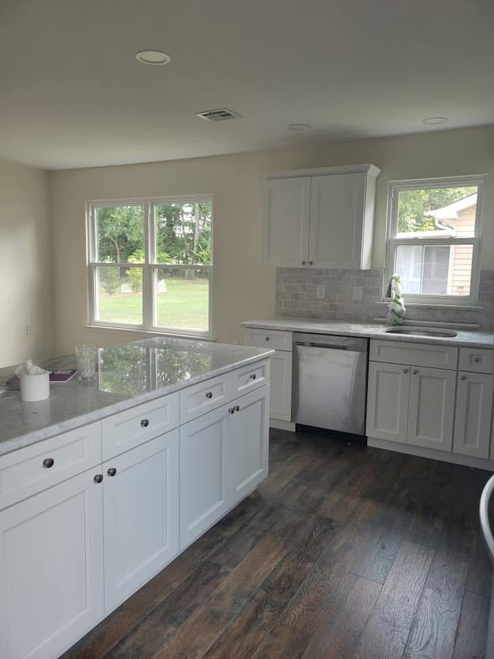 Bright kitchen with white cabinets, dark wood floor, island, and large windows overlooking a green yard