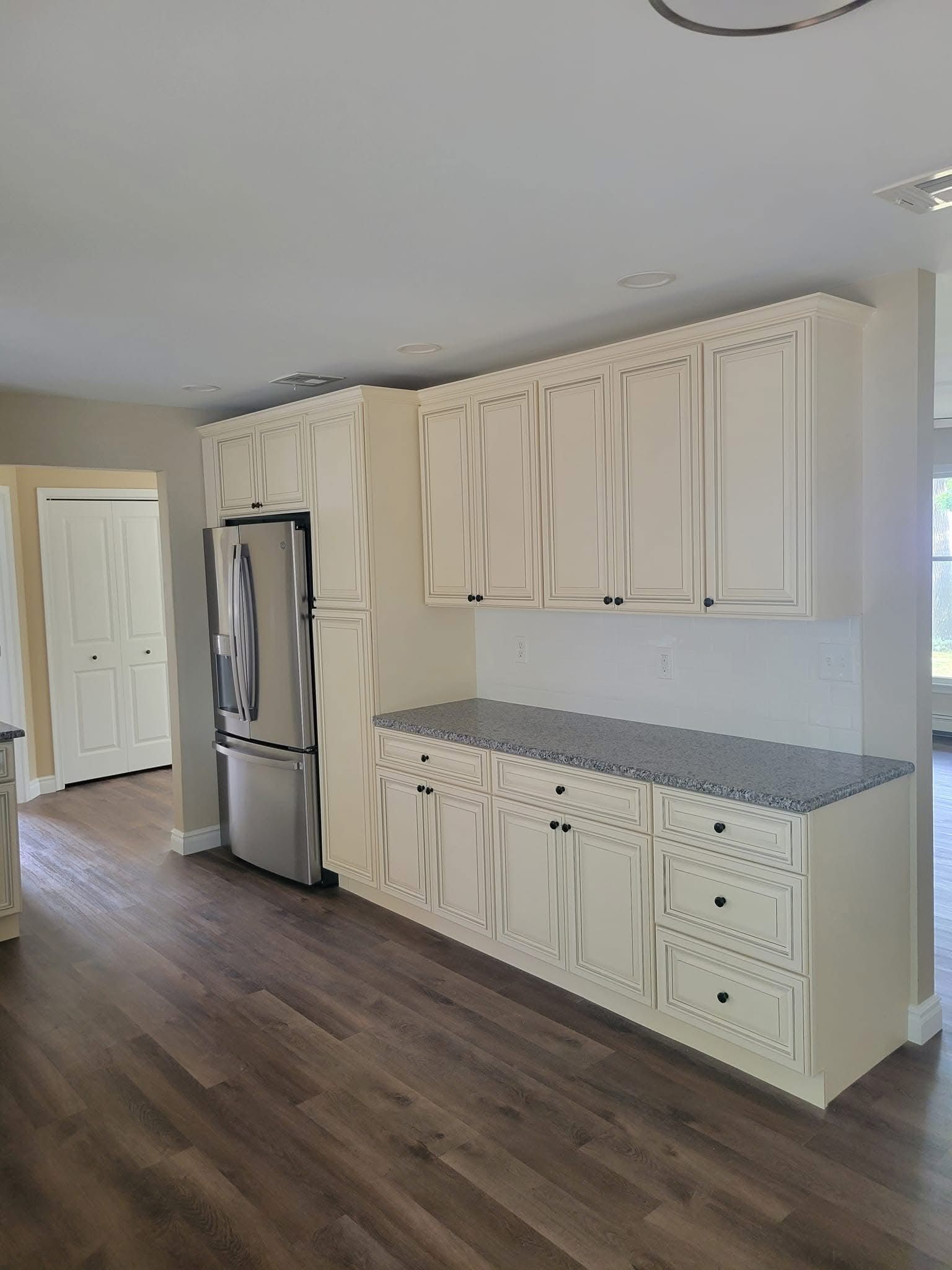 Bright kitchen with white cabinets, stainless steel fridge, gray countertops, and wood flooring