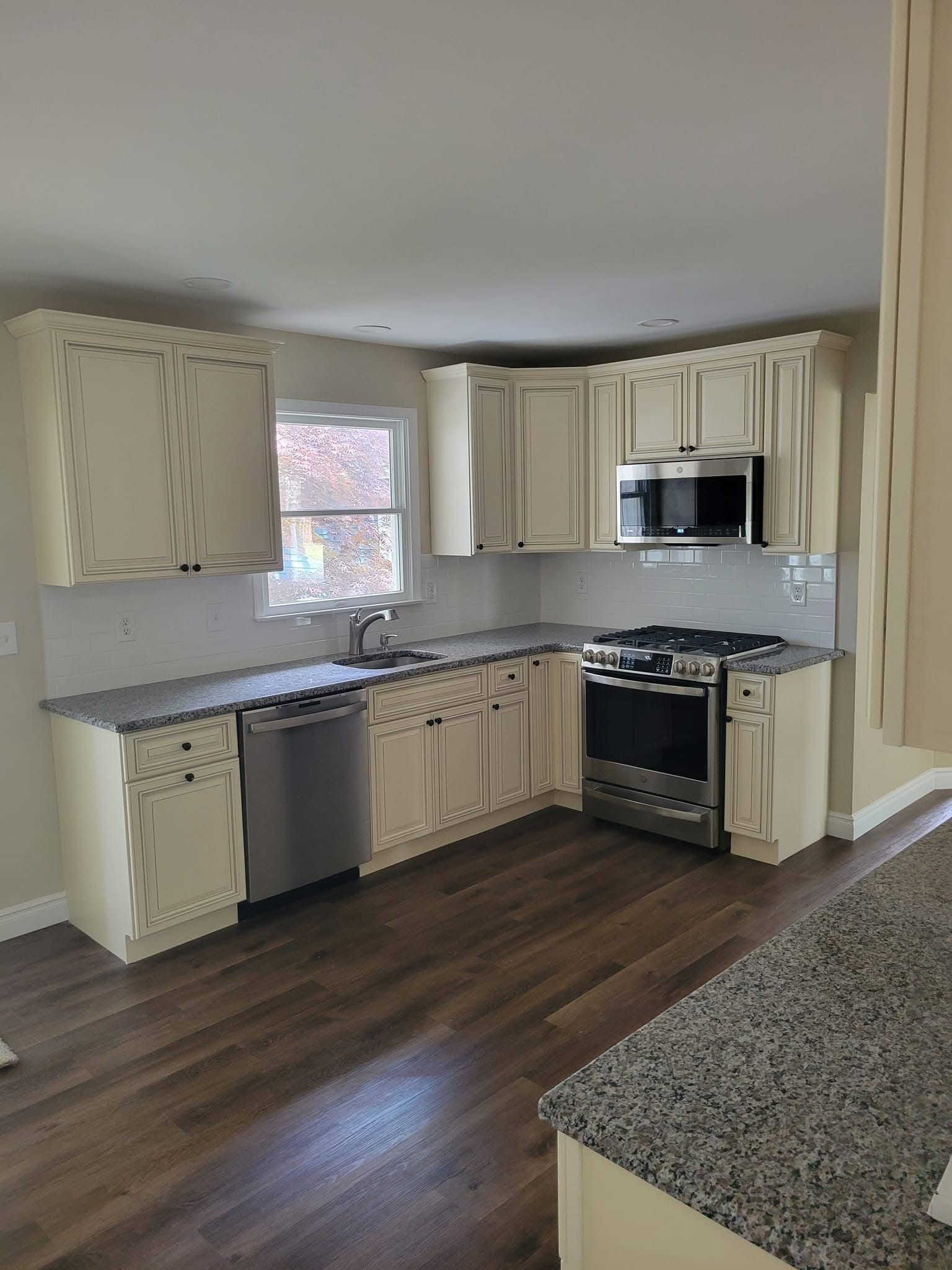 Empty kitchen with cream cabinets, stainless appliances, gray countertops, and dark wood floors.