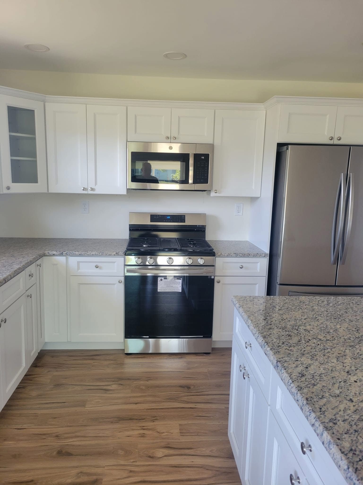 Bright white kitchen with stainless steel appliances, granite counters, and wood flooring.