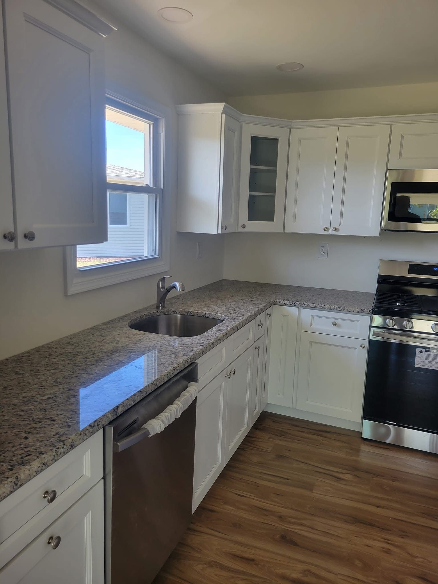 Bright kitchen with white cabinets, granite countertops, stainless dishwasher, and a window over the sink.