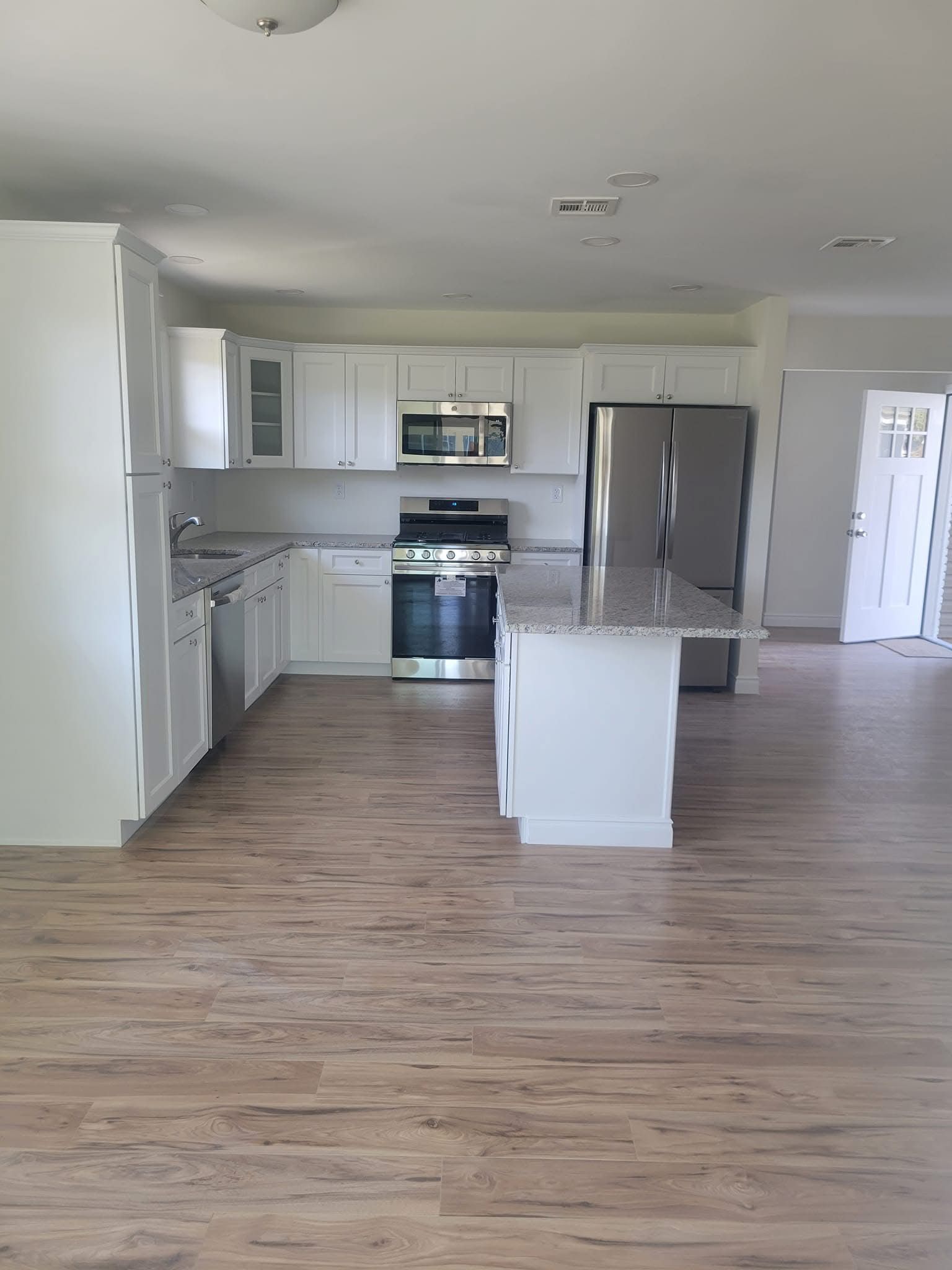 Spacious modern kitchen with white cabinets, stainless steel appliances, and light wood floors