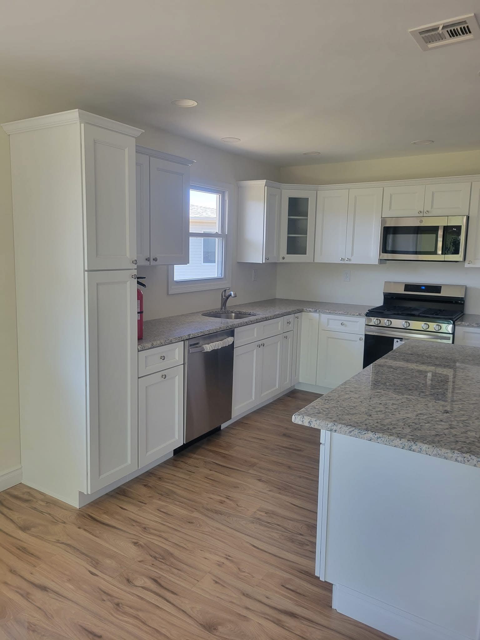 Bright white kitchen with granite counters, stainless appliances, and wood floors