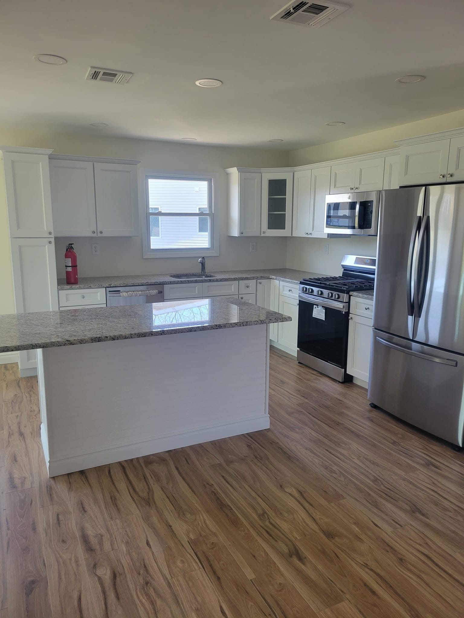 Bright modern kitchen with white cabinets, stainless steel appliances, granite island, and wood floors