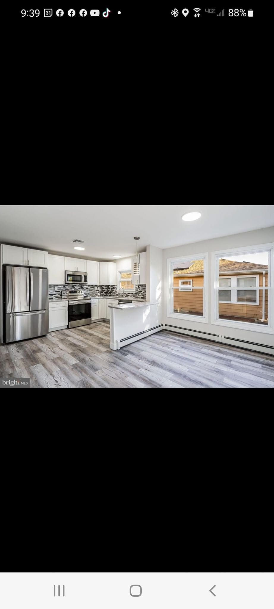 Bright modern kitchen with stainless steel fridge, white cabinets, island, and wood-look flooring.