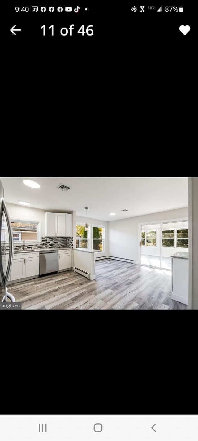 Bright empty modern kitchen and dining area with white cabinets, gray wood floors, and large windows