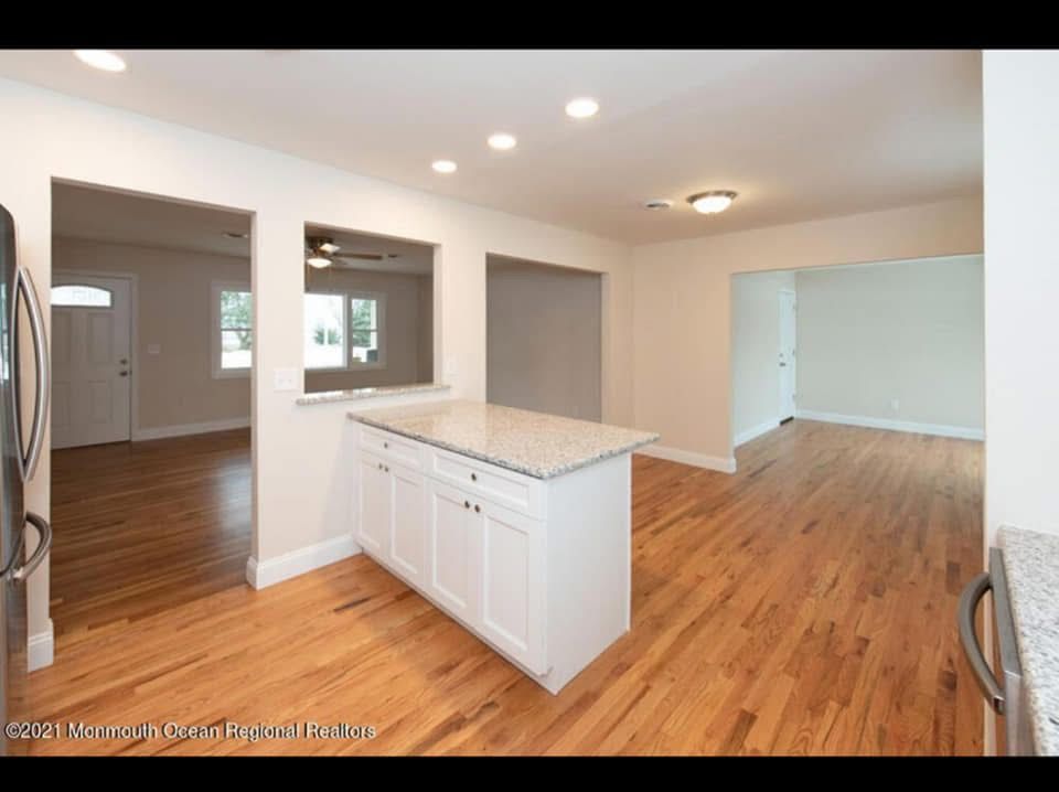 Bright empty kitchen with white island, hardwood floors, and open archway to adjacent rooms