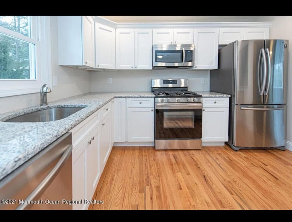 Bright modern kitchen with white cabinets, granite counters, stainless appliances, and wood floors