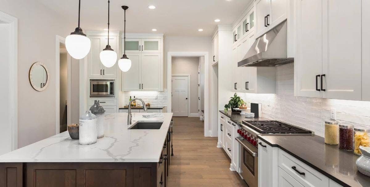 Bright modern kitchen with white cabinets, marble island, pendant lights, and stainless steel appliances