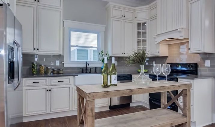 Bright white kitchen with island, marble counters, and wine glasses on the counter.