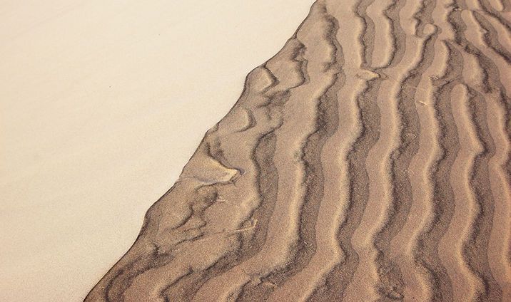 Close-up of sand dune ridges with wavy brown patterns beside smooth beige sand