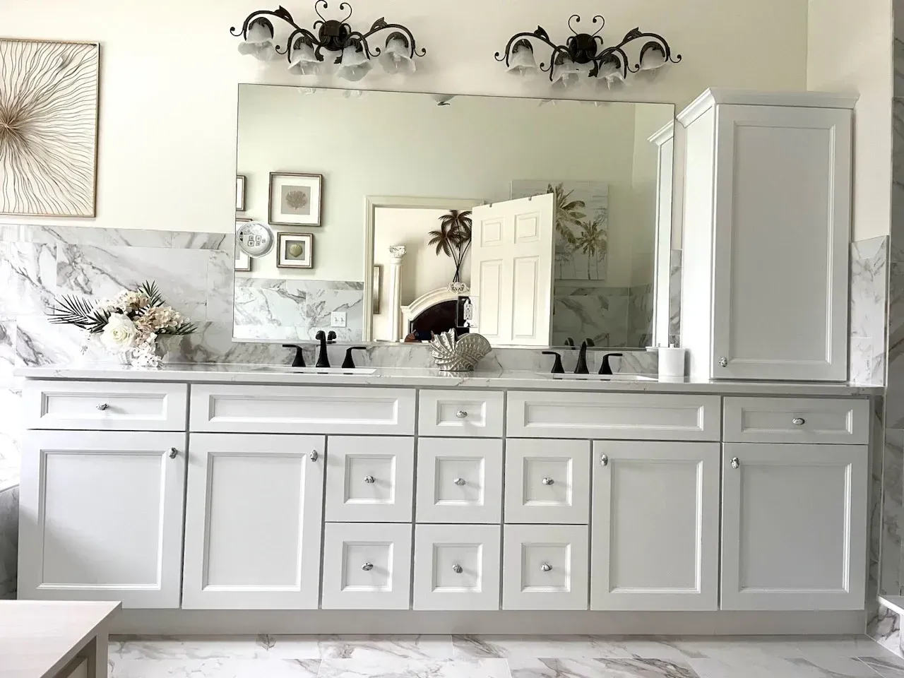 White bathroom vanity with double sinks, large mirror, and wall sconces in a bright neutral interior