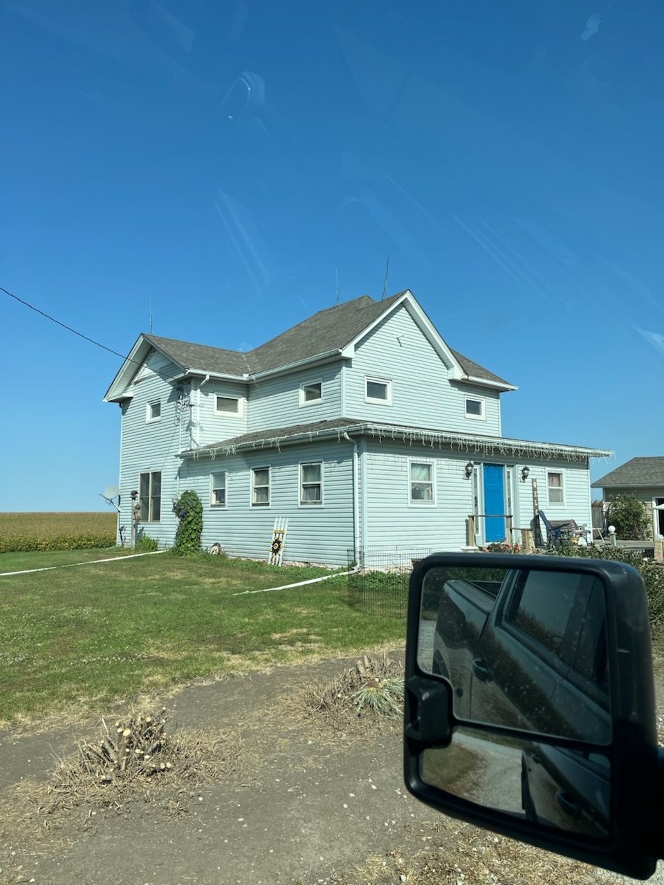 Light blue farmhouse with blue door on a grassy roadside under a clear blue sky