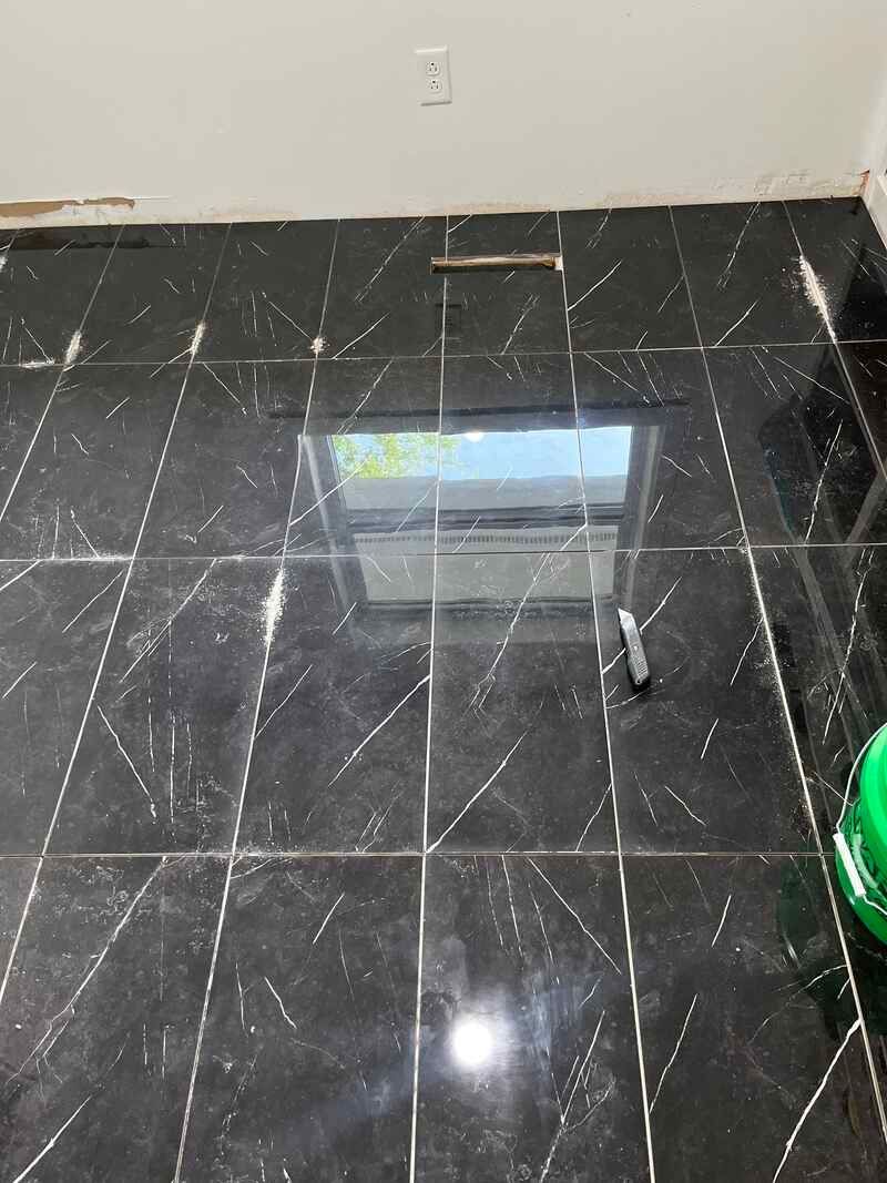 Glossy black tiled floor with window reflection, white wall, and a green object at the edge