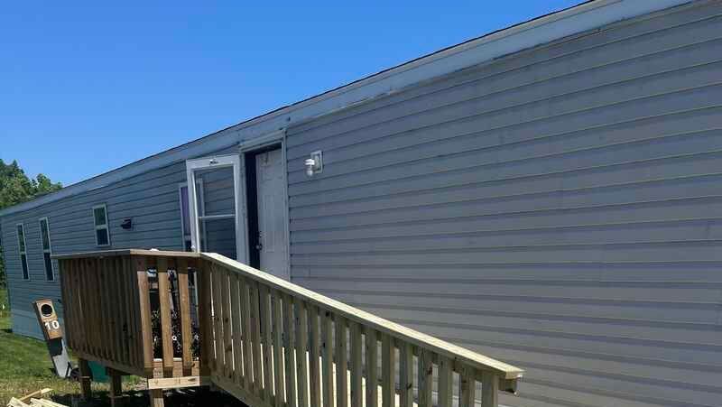 Mobile home exterior with wooden ramp and deck under a blue sky