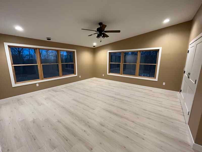 Empty beige bedroom with white wood floors, two windows, ceiling fan, and a closet door