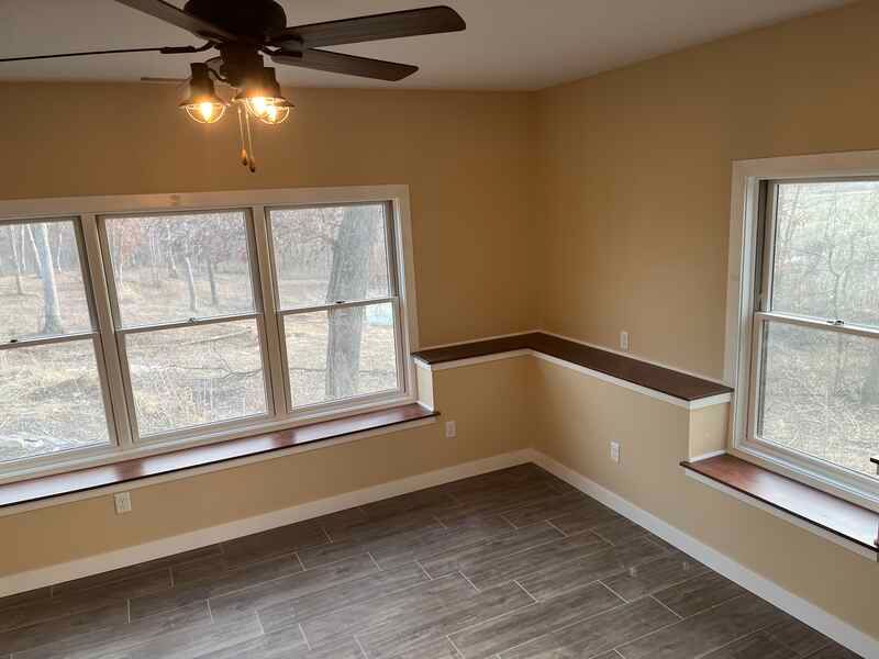 Empty beige room with large windows, dark wood floor, and ceiling fan.