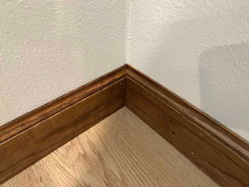Wooden baseboard corner on a light wood floor against a white wall