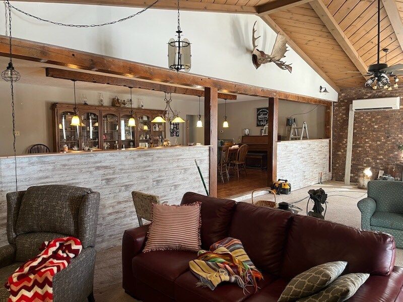 Rustic lodge-style living room with leather sofas, stone walls, wood beams, and warm lighting