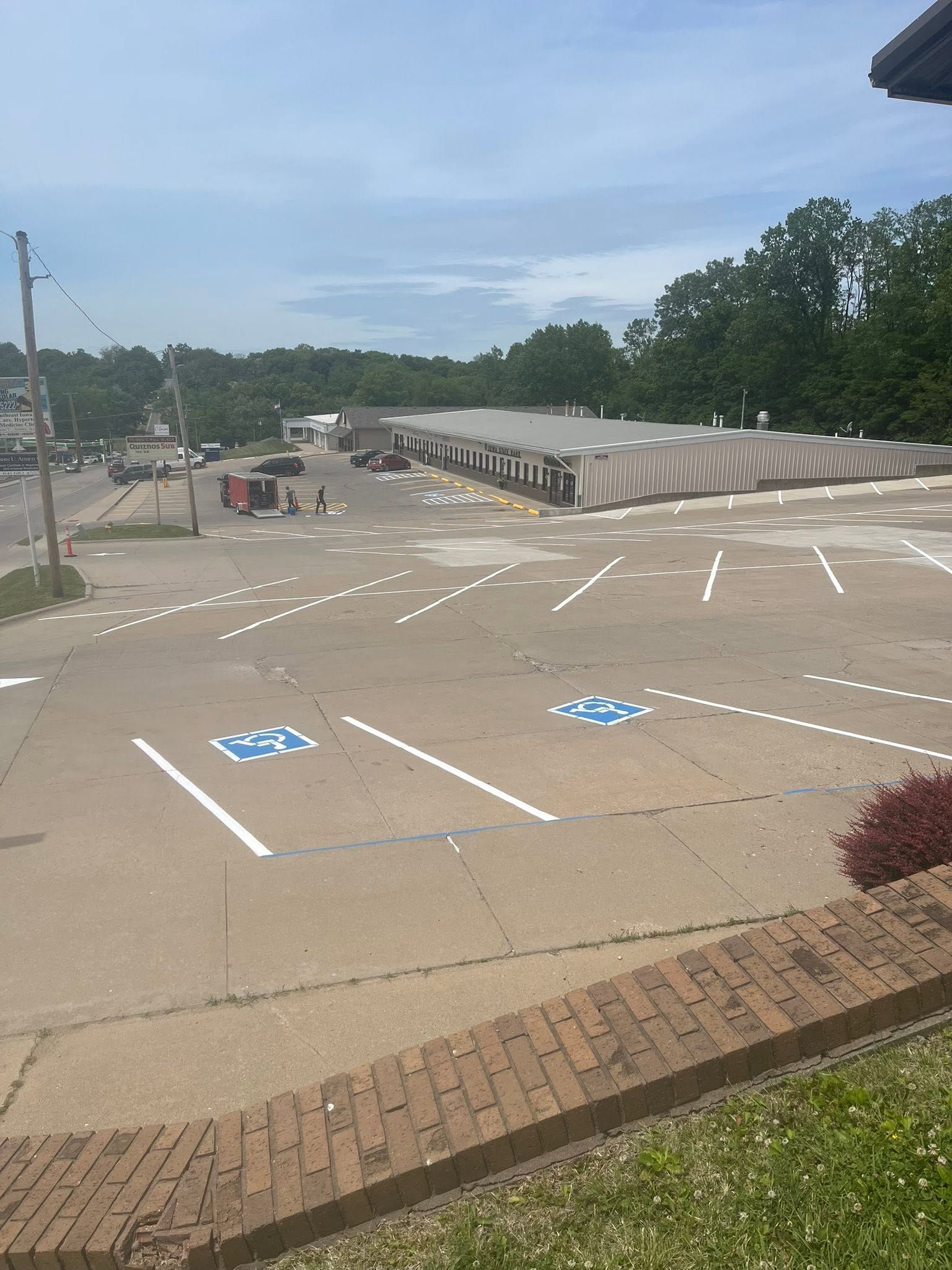 Empty parking lot with accessible spaces, concrete pavement, and trees under a blue sky