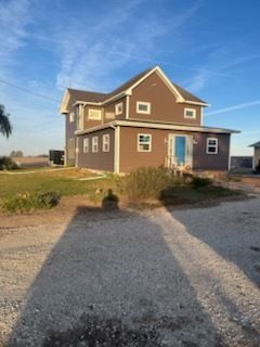 Two-story brown house with blue door and gravel driveway under a clear sky