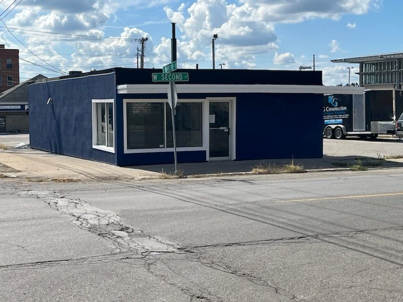 Blue storefront on a street corner under a cloudy sky, with a green street sign above the entrance