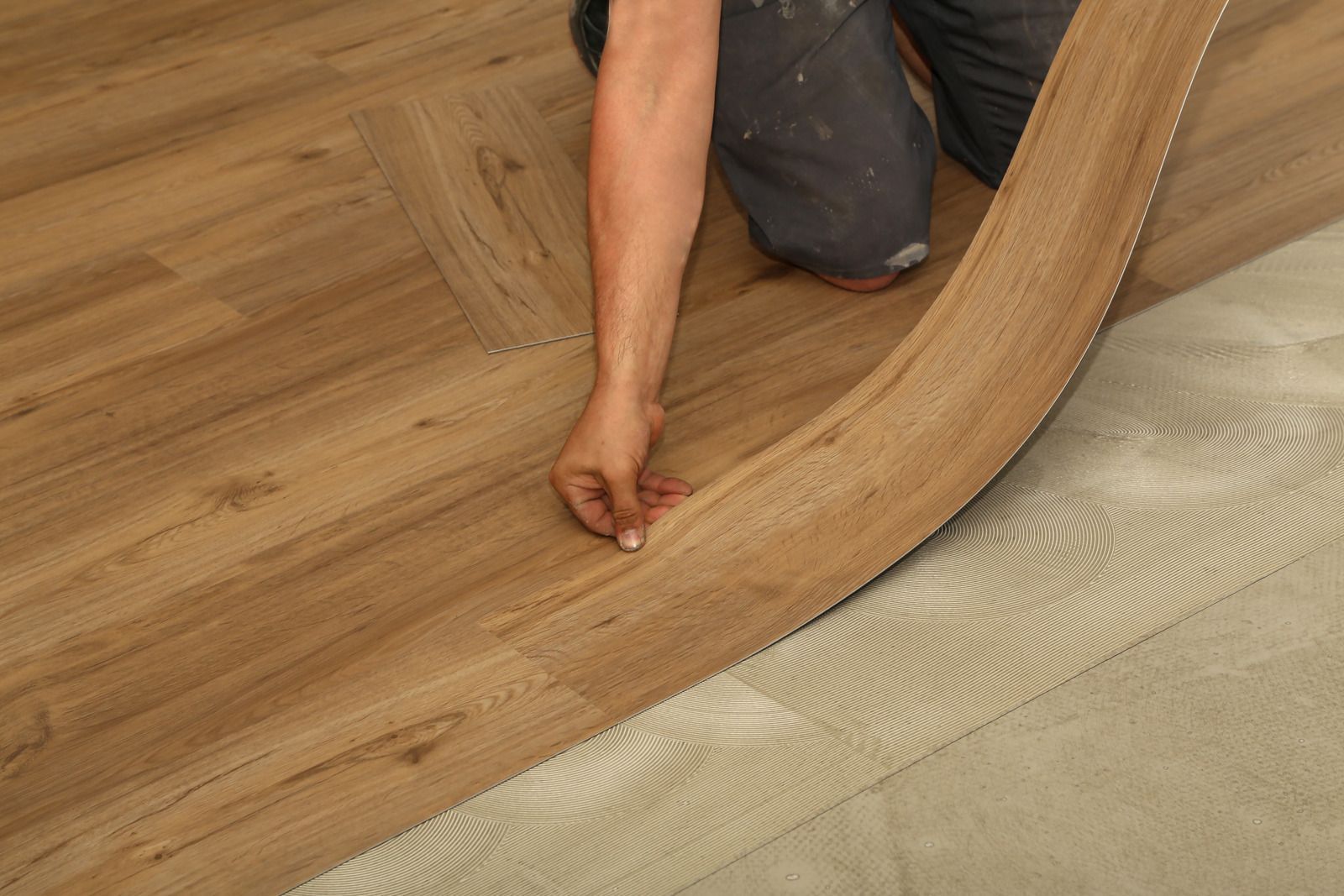 Person laying wood flooring, peeling back a curved plank over a gray underlayment.
