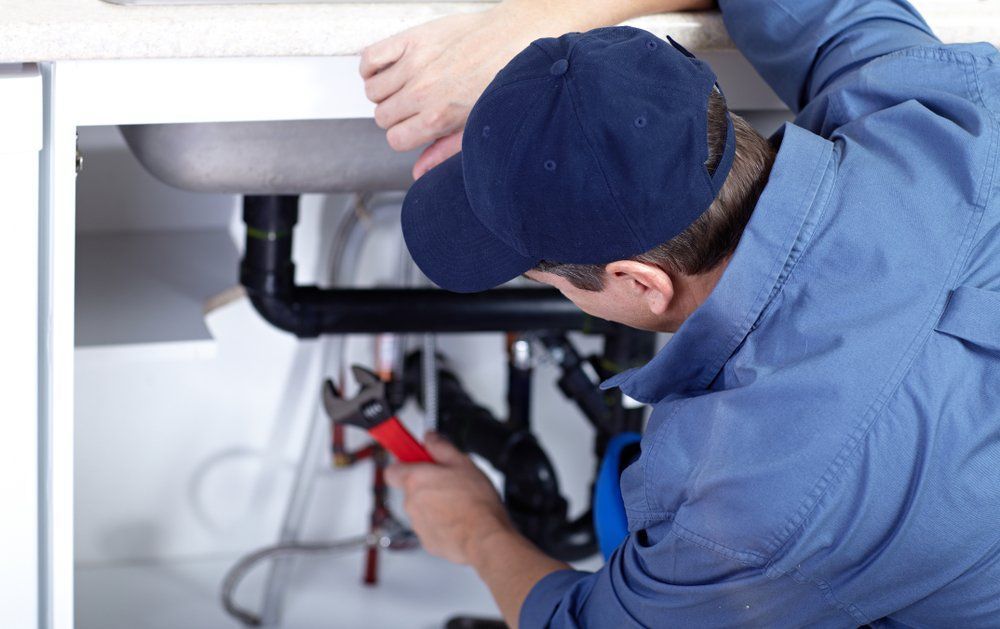 A Plumber is Fixing a Sink With a Wrench — SOS Hot Water & Plumbing Services in Kiama, NSW