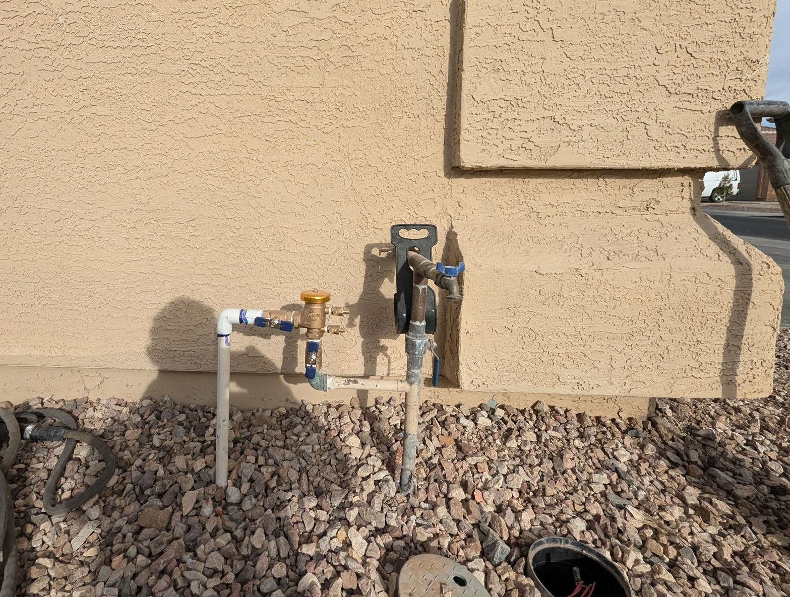 Outdoor gas and water meter valves on a stucco wall above gravel landscaping